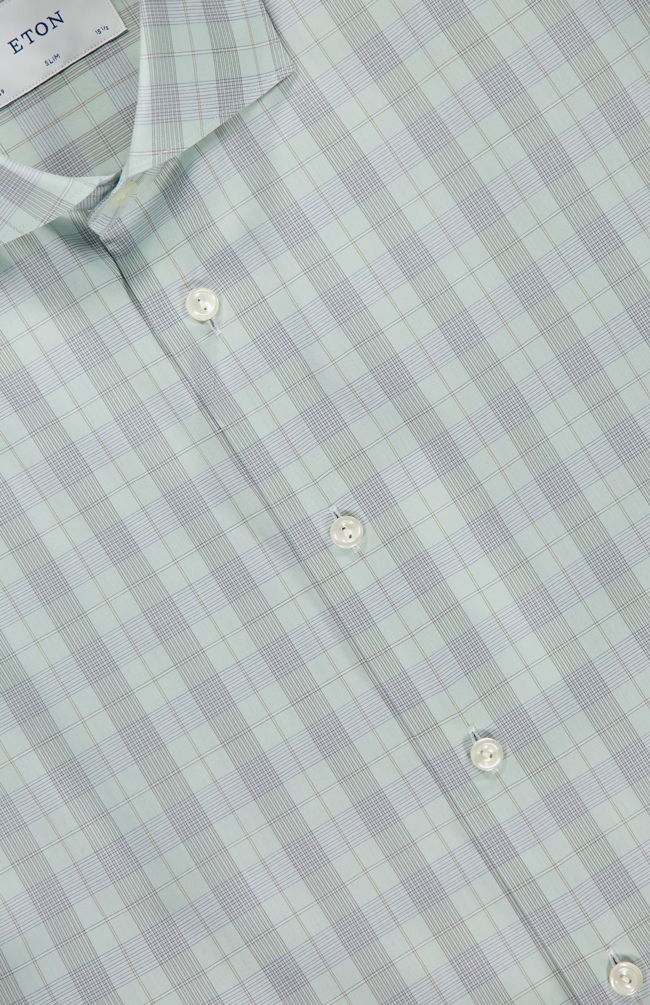 Close-up of the ETON Plaid Breeze Poplin Dress Shirt in light green plaid with white buttons and a pointed collar. The tag shows the ETON brand, emphasizing the modern, slim fit style.