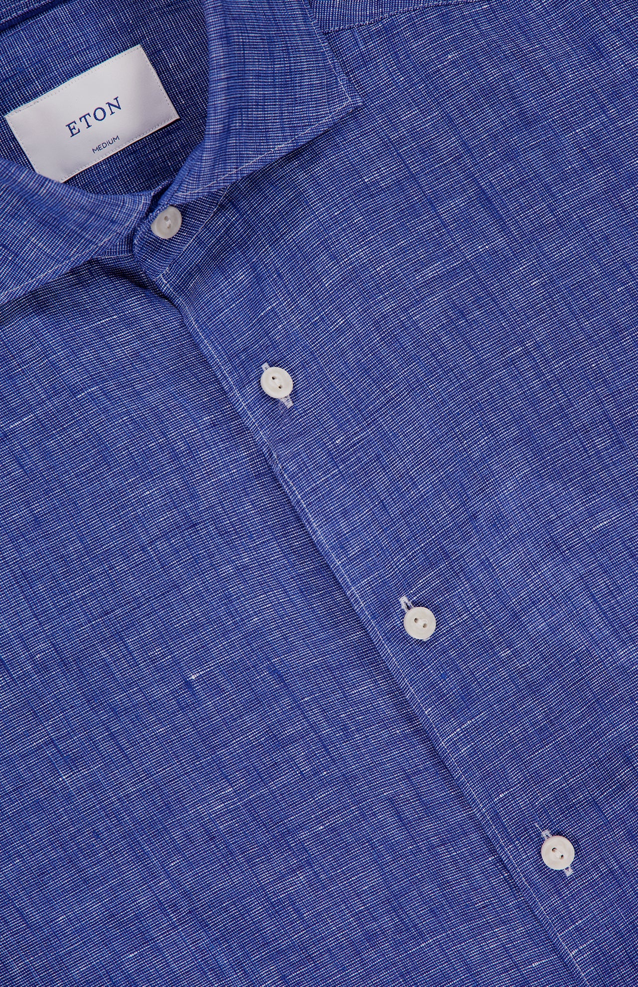 Close-up of a blue Solid Linen Dress Shirt by ETON, featuring white buttons and an inner collar label displaying ETON and MEDIUM—ideal for men’s summer wear.
