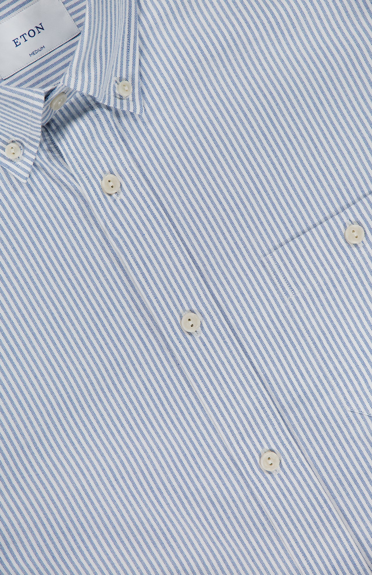 Close-up of ETON’s Striped Cotton Oxford Shirt, featuring light blue stripes, white buttons, and a visible chest pocket. Made from high-quality cotton, the shirt has an inner collar label displaying the ETON brand.