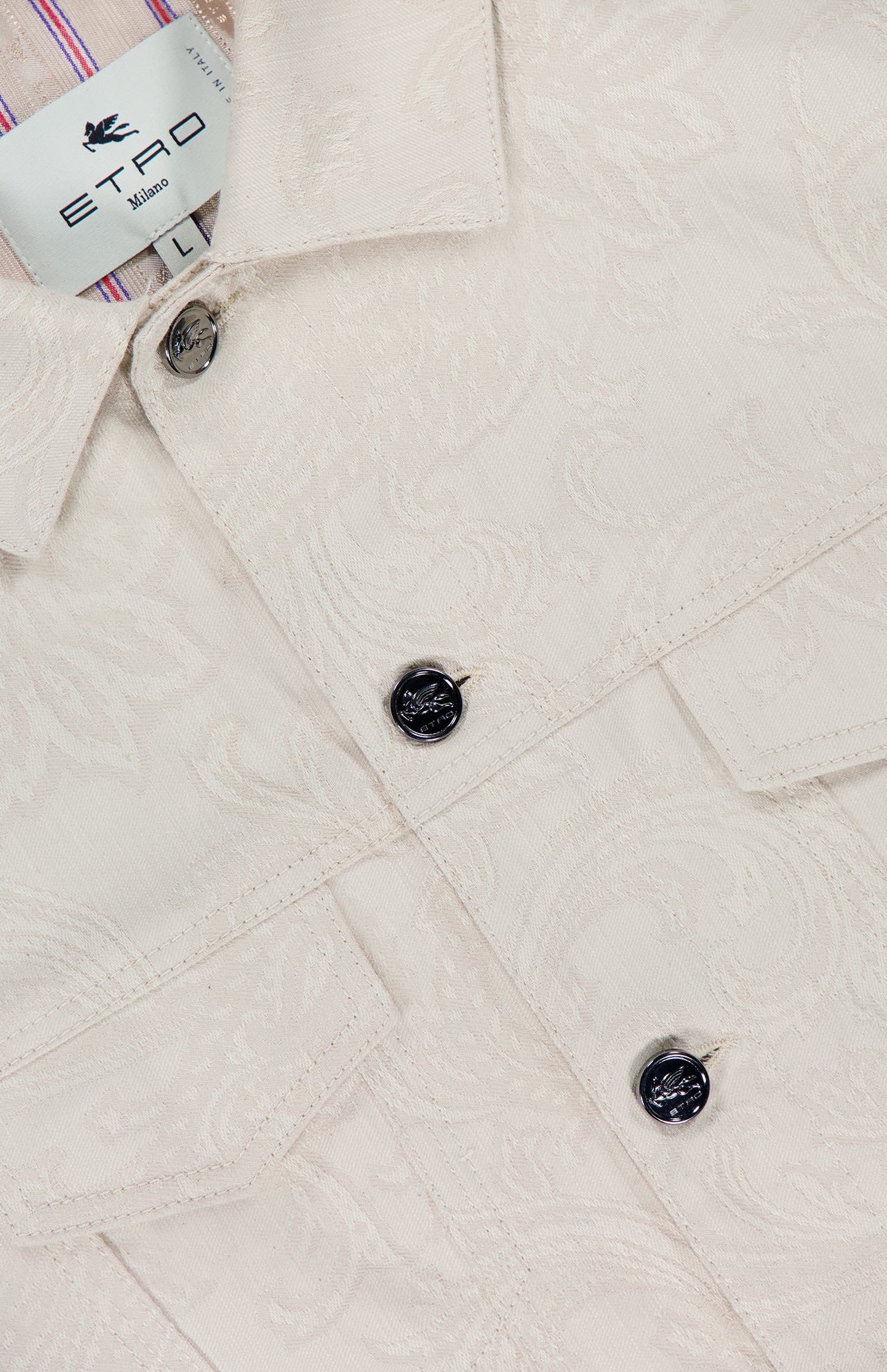 Close-up of ETRO’s Tonal Paisley Print Denim Jacket in cream, showcasing black buttons, flap chest pockets, and a striped collar lining. Made in Italy.