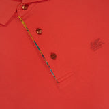 Close-up of ETRO's Roma Printed Detail Polo Shirt in vibrant tangerine, featuring a collar, two brown buttons, colorful inner placket, chest embroidered logo, and a partially visible neckline label.