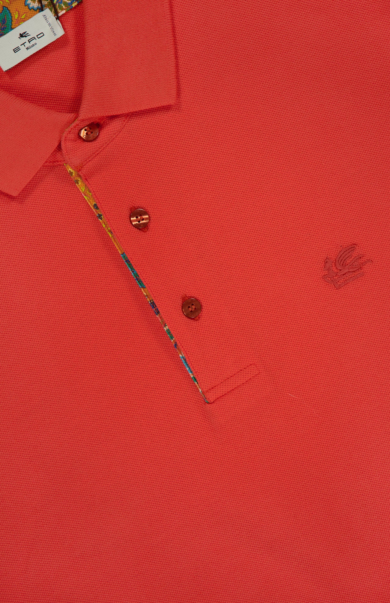 Close-up of ETRO's Roma Printed Detail Polo Shirt in vibrant tangerine, featuring a collar, two brown buttons, colorful inner placket, chest embroidered logo, and a partially visible neckline label.