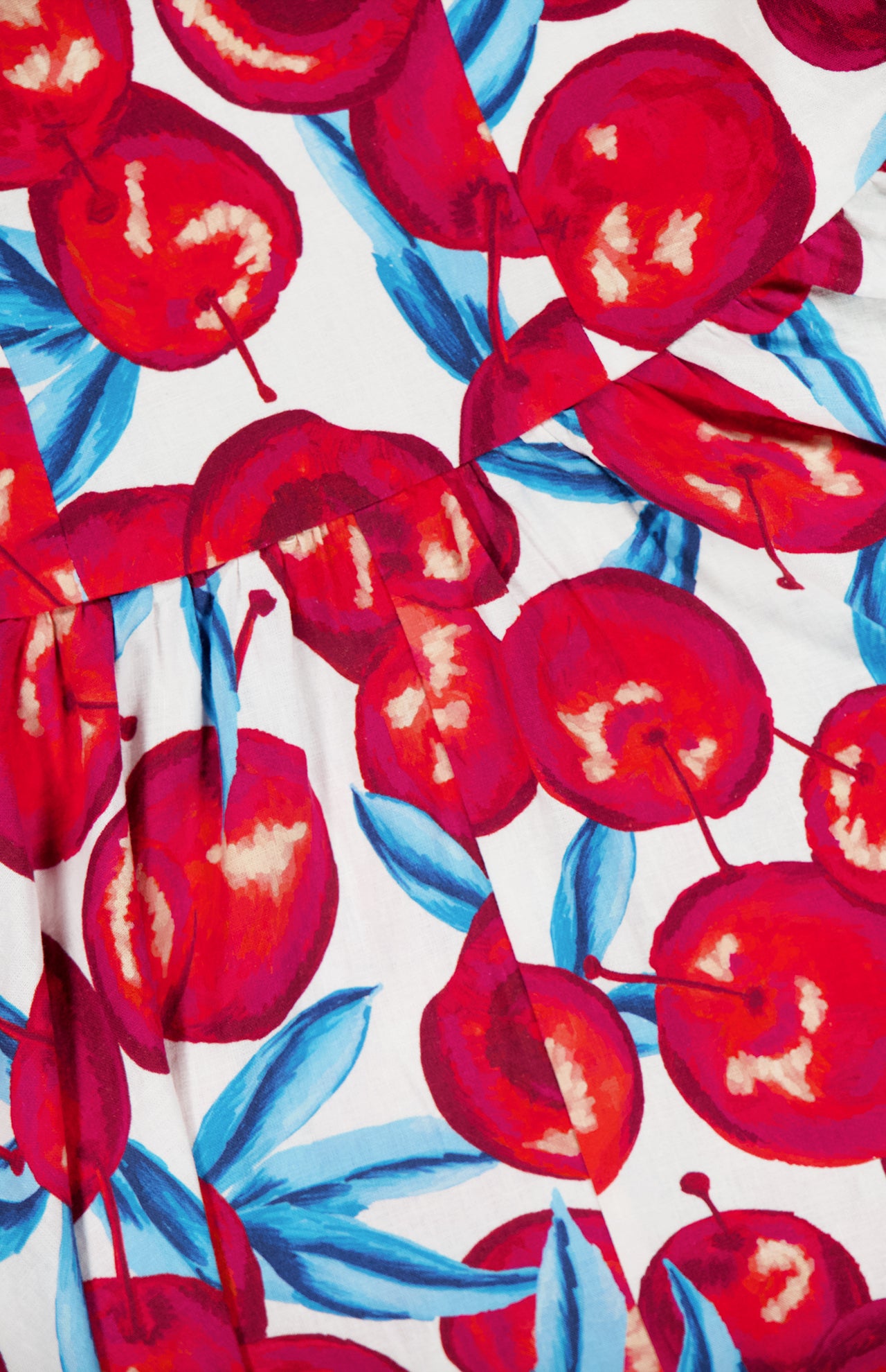 A close-up of the Cherry Blossom Sleeveless Midi Dress by FARM RIO shows its bold, artistic pattern: vibrant red cherries with blue leaves on white linen-blend fabric, adding playful charm to this stylish midi dress.