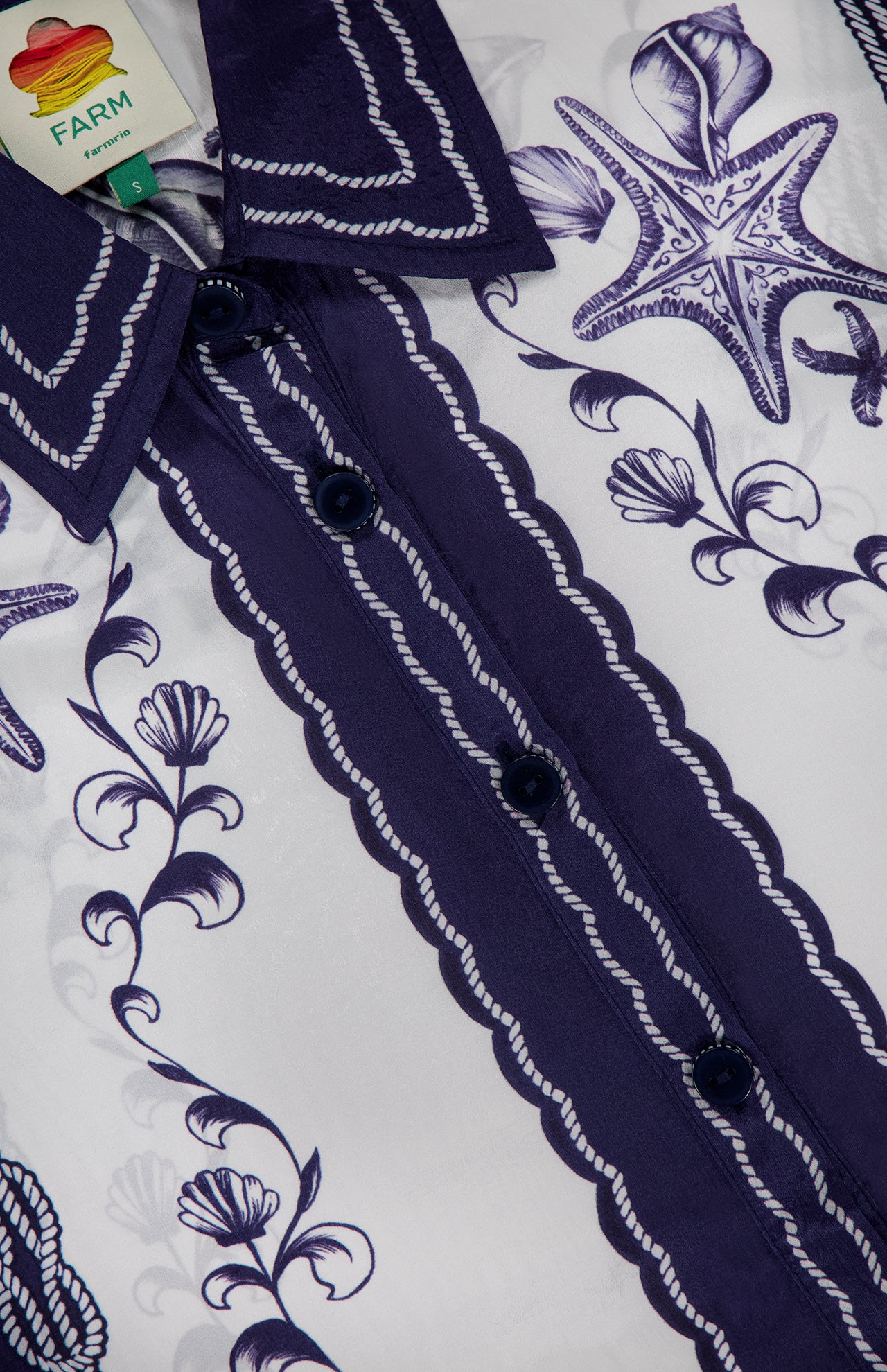 Close-up of the FARM RIO Coast Scarf Wide Sleeve Shirt in blue and white, featuring dark blue buttons and intricate ocean-inspired floral and starfish prints. Collared with a visible FARM RIO tag—perfect for vacation style.