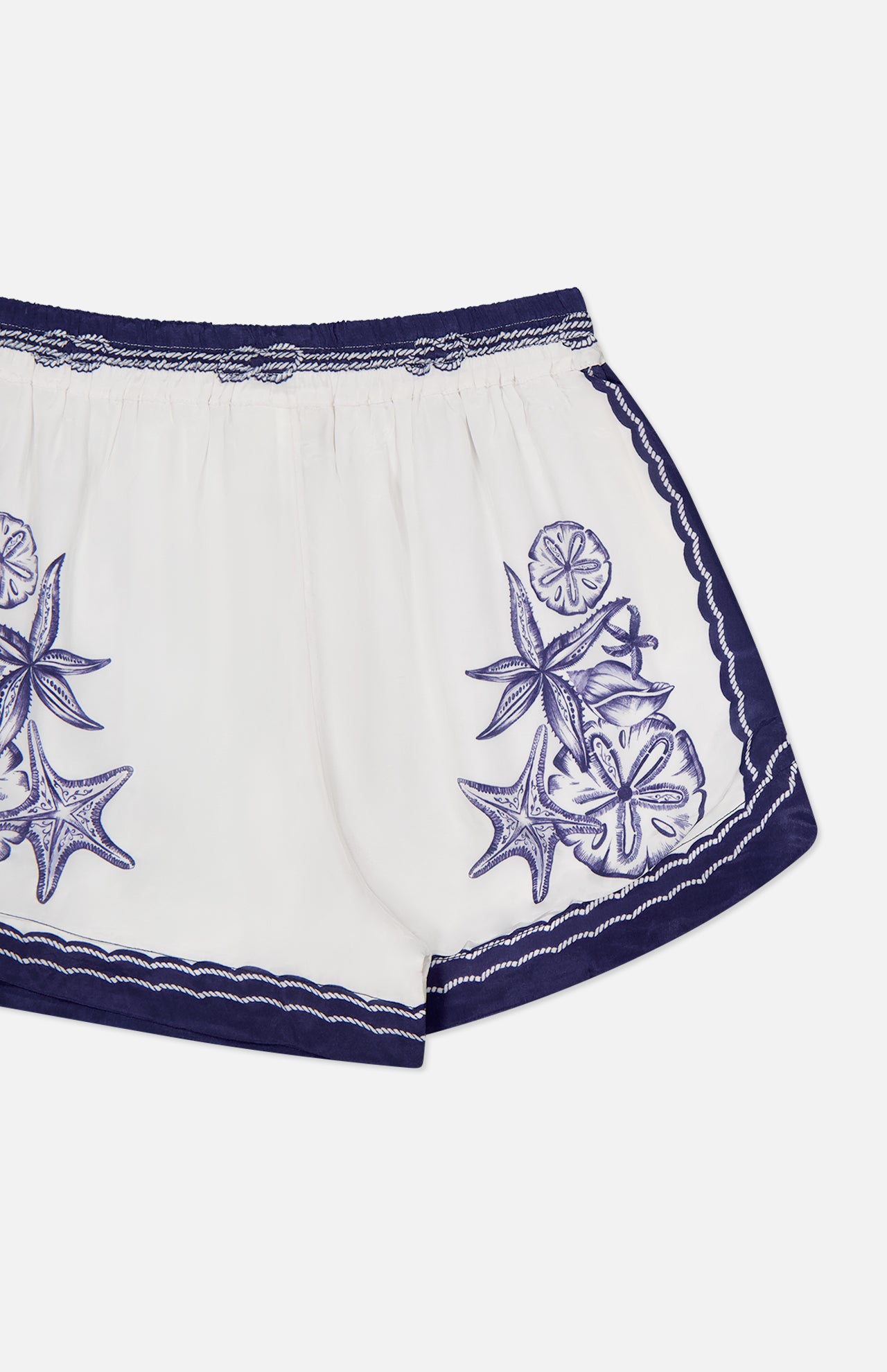 The Coast Scarf Shorts by FARM RIO showcase a dark blue waistband and hem, with embroidered sea star and sand dollar accents. The image highlights the upper half on a clean white background—ideal for coastal getaways.
