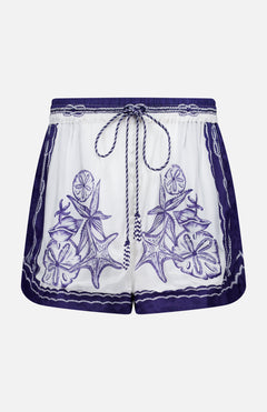 The Coast Scarf Shorts by FARM RIO are white coastal vacation shorts with a navy waistband, blue floral and leaf embroidery on the front, borders, and a braided drawstring tie at the waist.