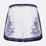 FARM RIO's Coast Scarf Shorts are white coastal vacation shorts with an elastic waistband, purple embroidered seashell and starfish accents on each side, and a purple scalloped trim along the waistband and hem.