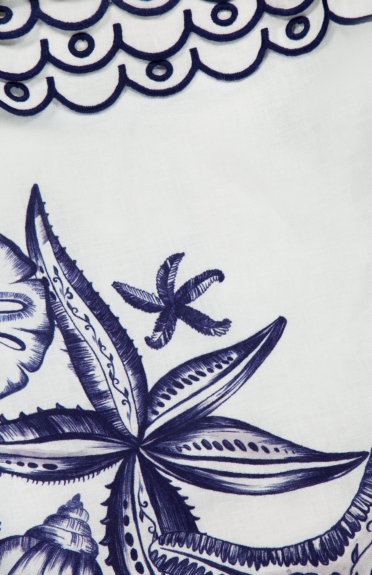 A close-up of the Coast Stars Linen Mini Dress by FARM RIO, featuring white linen embroidered with navy seashells, starfish, and scalloped wave patterns—ideal for a chic coastal party look.