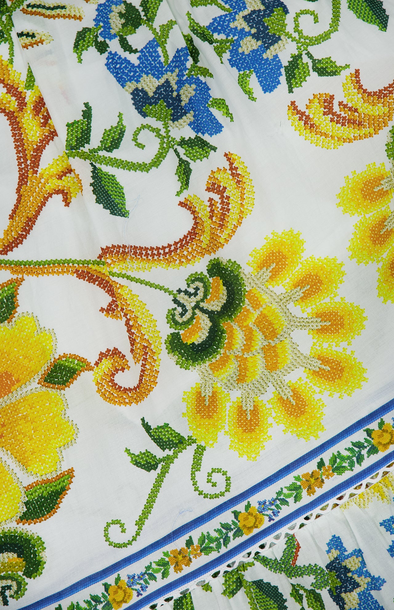 Close-up of the Emily Floral Tapestry Midi Dress by FARM RIO, featuring vibrant yellow, green, and blue floral embroidery on white fabric with blue and green borders—ideal for adding artistic charm to your summer or boho wardrobe.