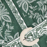 Close-up of the FARM RIO Miranda Short Sleeve Belted Romper, featuring green tropical floral and leaf prints, a belted waist with a round off-white woven buckle, intricate designs, and detailed stitching.