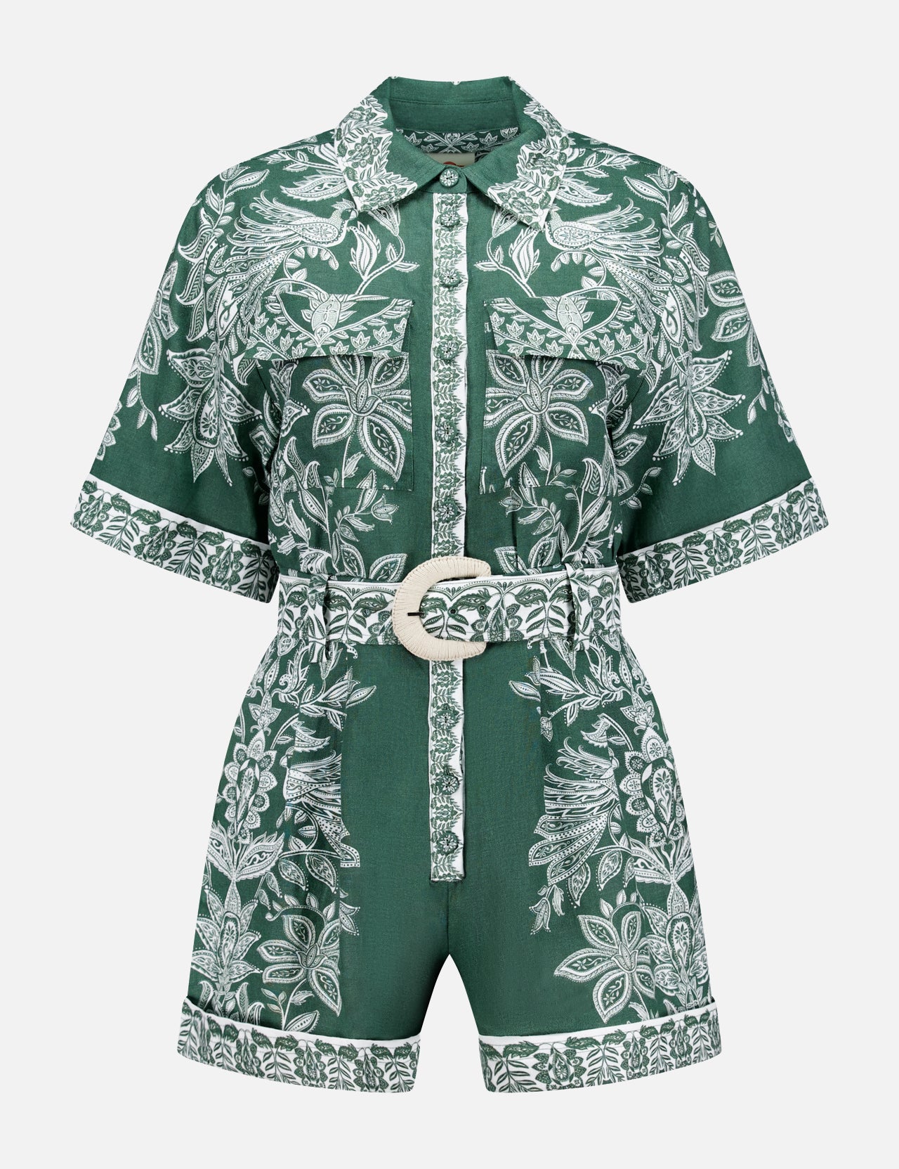 The Miranda Short Sleeve Belted Romper by FARM RIO features green fabric with white floral patterns, a collared neckline, front buttons, and a matching belt with a round buckle. Floral trim accents the hem and button placket.