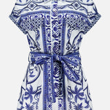 The FARM RIO Wonderful City Linen Romper features short sleeves, a collared neckline, a blue and white nature-inspired floral and geometric print, a button-down front, and a matching fabric belt at the waist.
