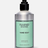 A silver pump bottle of FLAMINGO ESTATE Jasmine Damask Rose Hand Soap, with a mint green label featuring black text and a decorative border. The label highlights nourishing rosehip seed oil. The background is plain light gray.