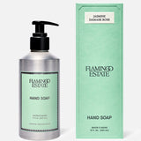 A silver pump bottle of FLAMINGO ESTATE Jasmine Damask Rose Hand Soap stands beside its matching green box, both featuring minimalist black text and enriched with nourishing rosehip seed oil on a light green background.