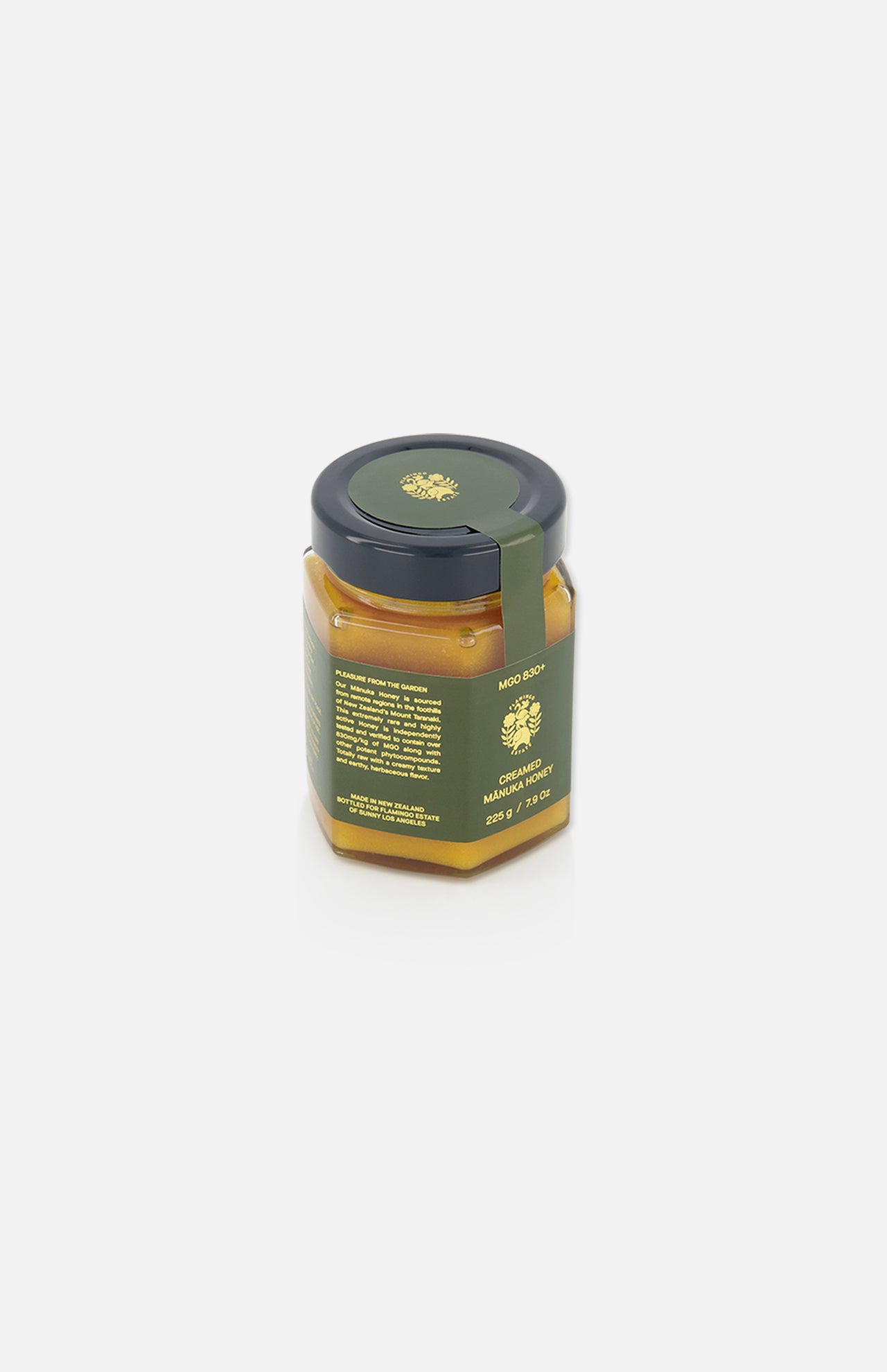 A hexagonal glass jar with a dark green lid, filled with creamy yellow content, labeled “Creamed Manuka Honey” (220g) by FLAMINGO ESTATE. The green label with yellow text and logo references Mānuka honey, set against a plain white background.