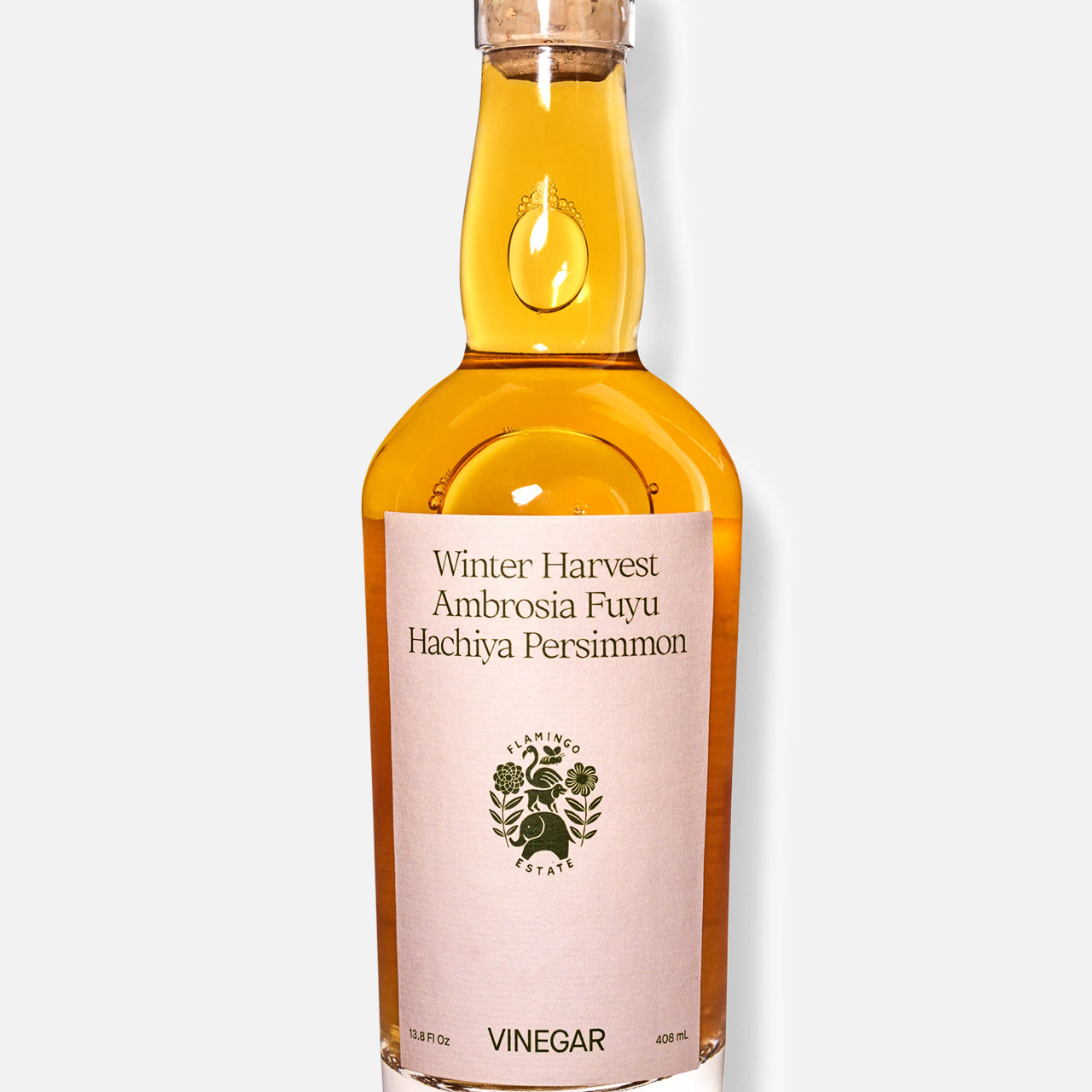A clear glass bottle of FLAMINGO ESTATE Persimmon Vinegar contains amber liquid and features a tree logo, black text on a cream label reading Winter Harvest Ambrosia Fuyu Hachiya Persimmon, plus a dark cap, set against a white background.