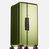 The Bold Suitcase by FLOYD is a metallic green hard-top case with a black handle and lock, featuring signature skateboard-inspired red transparent spinner wheels, shown upright against a plain white background.