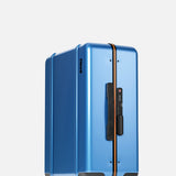 The Cabin Suitcase by FLOYD is a modern blue hard-top suitcase with a black side handle, yellow zipper, TSA lock, and four red transparent skateboard spinner wheels, shown standing upright against a plain white background.