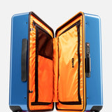 The FLOYD Cabin Suitcase features a blue hard-top shell, bright orange interior with mesh and zippered compartments, skateboard-style spinner wheels with branding, and a built-in TSA lock on the side.