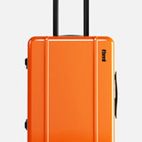 The Cabin Suitcase by FLOYD is a bright orange hard-top suitcase with a black telescopic handle and two red skateboard spinner wheels, shown standing upright against a plain white background.