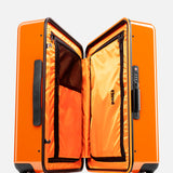 The Cabin Suitcase by FLOYD is shown upright and open, displaying its orange interior with zippered compartments and mesh pockets. It features a bright orange hard-top shell, black handles, and four skateboard spinner wheels with red FLOTE accents.