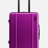 The Cabin Suitcase by FLOYD is a hard-shell, bright purple suitcase with a black handle, red 360° spinner wheels, and a small black logo, shown standing upright against a plain white background.