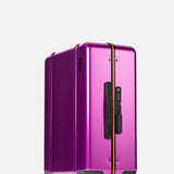 The Cabin Suitcase by FLOYD features a glossy purple hard-top, black handle, orange zipper, built-in TSA lock, and four red translucent 360° spinner wheels, showcased against a plain light background.
