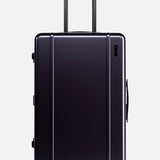 The Check-In Suitcase by FLOYD features a hard-top design in a dark hue, TSA lock, telescoping handle, and four red 360° spinner wheels. It is pictured upright against a plain light background.