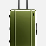 The FLOYD Check-In Suitcase features a green hard-top design, black handles, a secure TSA lock, and four red skateboard spinner wheels. It stands upright on a white background.