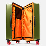 The FLOYD Check-In Suitcase features a green hard-top design, skateboard spinner wheels, and a bright orange interior with zippered compartments, mesh pockets, and a TSA lock.