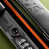 Close-up of The Check-In Suitcase by FLOYD: a black hard-top lock with a combination dial, "LOCK" and "TSA007" printed nearby, FLOYD engraved on the handle, plus an orange accent strip beneath.