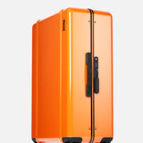The FLOYD Check-In Suitcase, a vibrant orange hard-top case with black trim and TSA lock, stands upright on four red transparent skateboard spinner wheels against a plain white background.