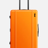 The FLOYD Check-In Suitcase is an upright, hard-top orange luggage with four pink skateboard spinner wheels, a black side handle, and an extended telescopic handle, shown against a plain white background.