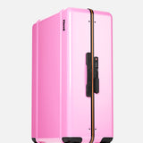 The Check-In Suitcase by FLOYD features a pink hard shell, black handles, a vertical black and yellow stripe, TSA lock, and four red transparent 360° spinner wheels. Shown on a plain white background.