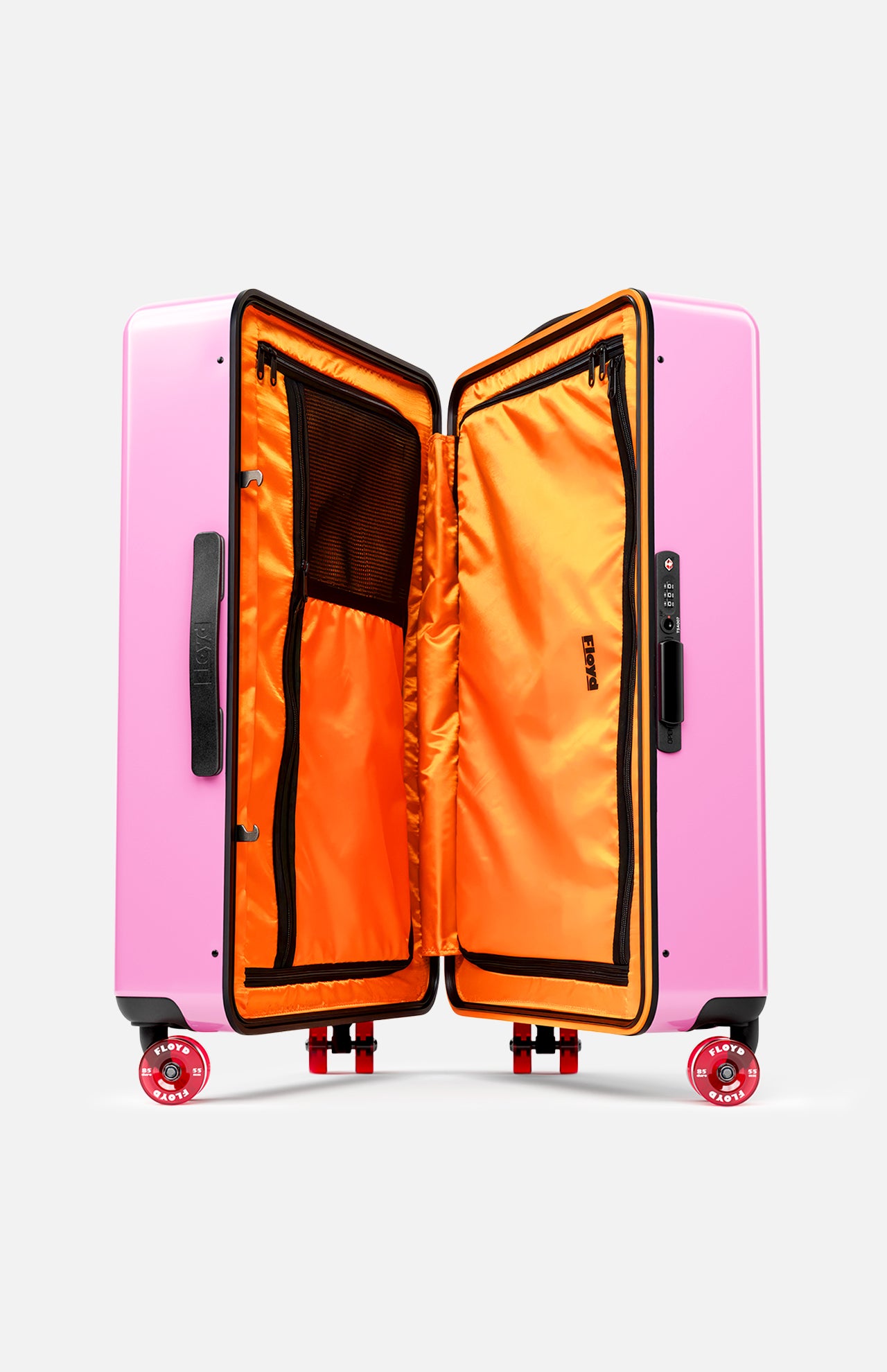 The FLOYD Check-In Suitcase features a hard pink shell, a vibrant orange interior with zippered mesh compartments, black handles, and four 360° spinner wheels.