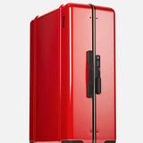 Standing upright against a light gray background, the FLOYD Check-In Suitcase features a sleek, shiny red hard-top design accented by a central gold and black stripe, four skateboard-style spinner wheels, and a black handle.