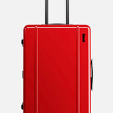 The Check-In Suitcase by FLOYD is a sleek, hard-top red suitcase featuring black handles and four red skateboard spinner wheels, pictured standing upright against a plain light background.