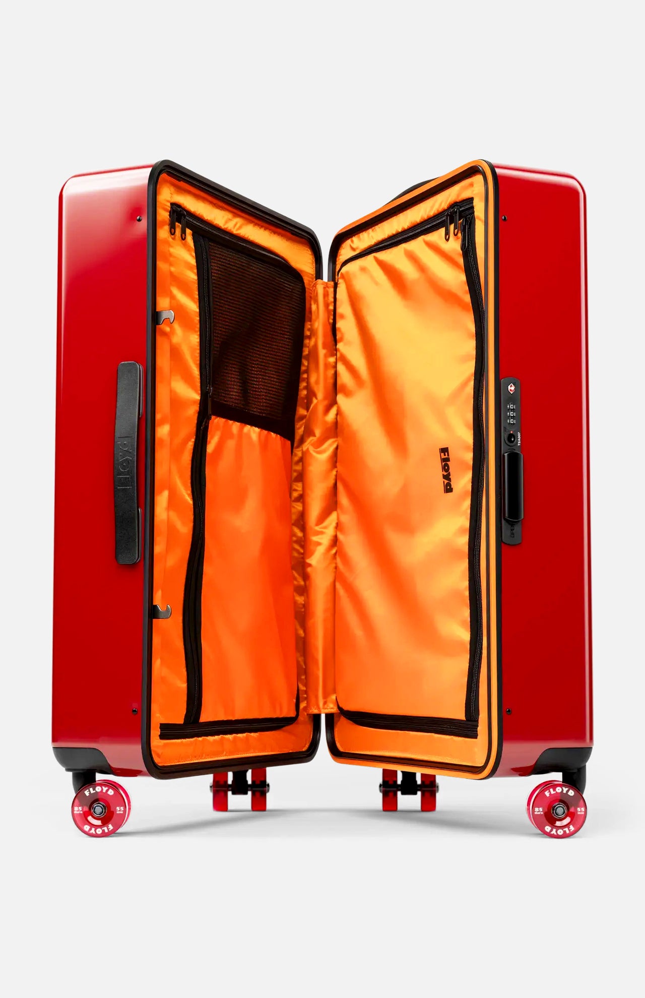 The FLOYD Check-In Suitcase stands upright with its hard red shell open to showcase a vibrant orange interior featuring mesh zippered compartments and a built-in TSA lock on the side. Designed for smooth mobility, it comes equipped with four skateboard spinner wheels and sturdy black handles.