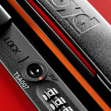 Close-up of a black TSA lock on a red FLOYD The Check-In Suitcase, showing the lock dial, zipper pull, and part of the FLOYD logo embossed on the case.