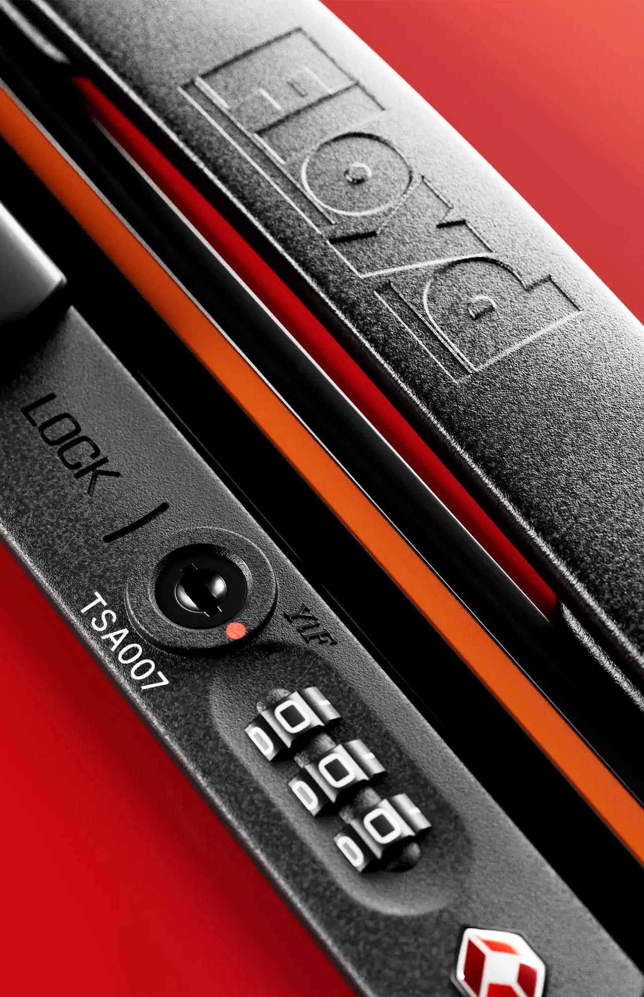 Close-up of a black TSA lock on a red FLOYD The Check-In Suitcase, showing the lock dial, zipper pull, and part of the FLOYD logo embossed on the case.