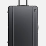 The Trunk Suitcase by FLOYD is a hard-top, dark gray suitcase featuring four red skateboard spinner wheels, a black side handle, and an extended black telescopic handle, displayed on a plain white background.