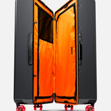 The Trunk Suitcase by FLOYD stands upright, open to display its vivid orange interior with mesh pockets and dividers. Shown on a white background, it features skateboard spinner wheels and a side handle.