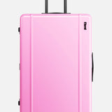 The Trunk Suitcase by FLOYD is a hard-top, pink rolling suitcase with a black handle and four 360° spinner wheels, pictured upright against a plain white background.
