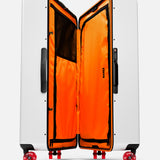 The Trunk Suitcase by FLOYD is a white hard-top check-in case with red skateboard spinner wheels, a sturdy black side handle, and an open bright orange interior featuring mesh pockets and black zippers.