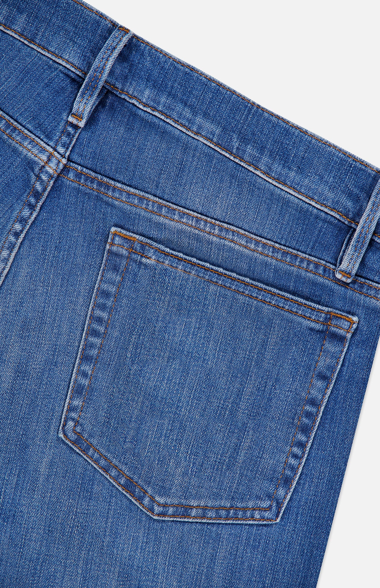 Close-up of the back pocket and waistband of the Frame L’Homme Slim Jean in Verdugo, highlighting the premium stretch denim’s visible stitching and belt loop. These dark blue jeans feature a subtle faded texture.