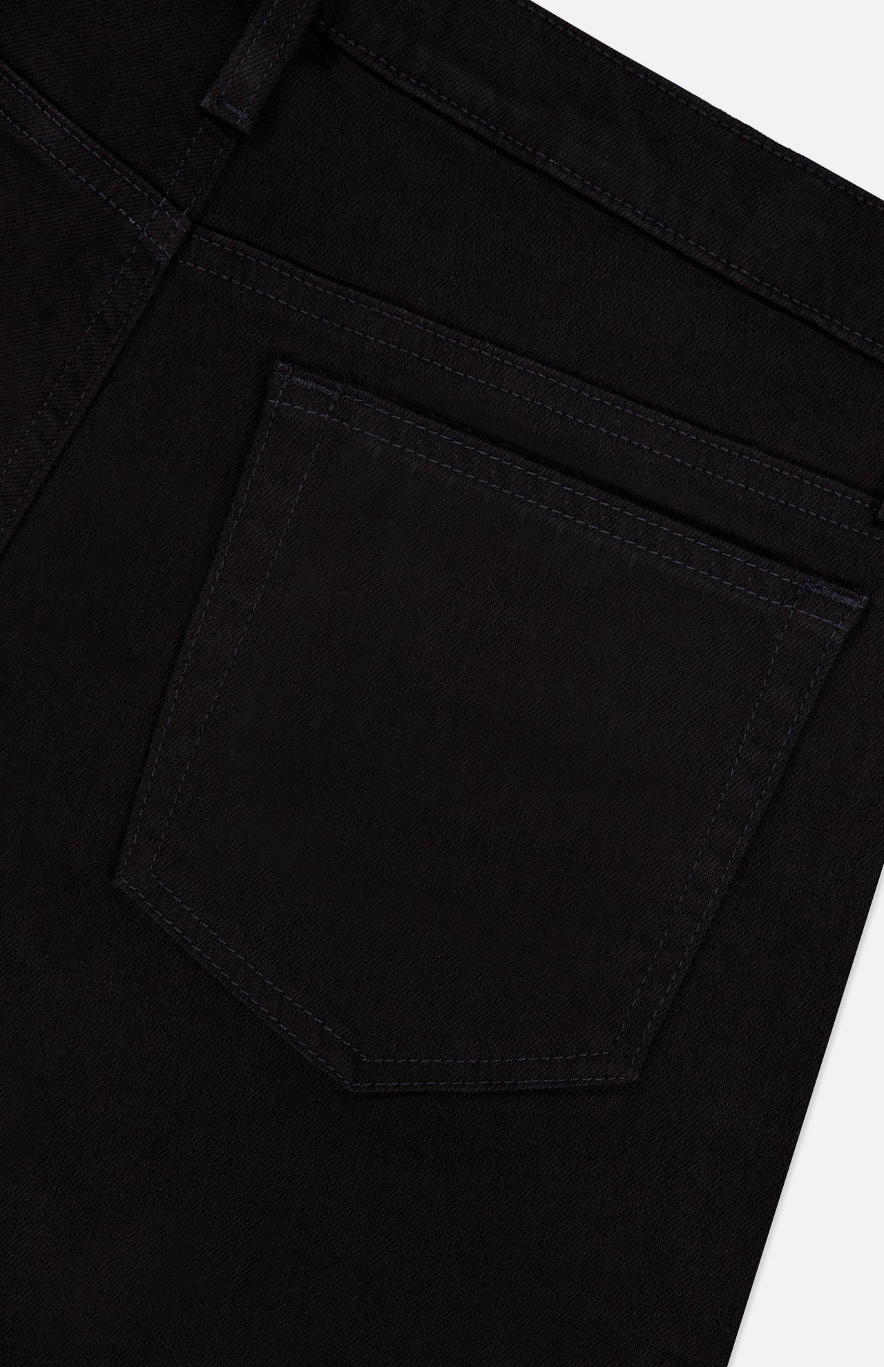Close-up of the back pocket of Frame’s L’Homme Slim Pant in Noir, crafted from stretch denim with dark stitching and a glimpse of the waistband, set against a white background.