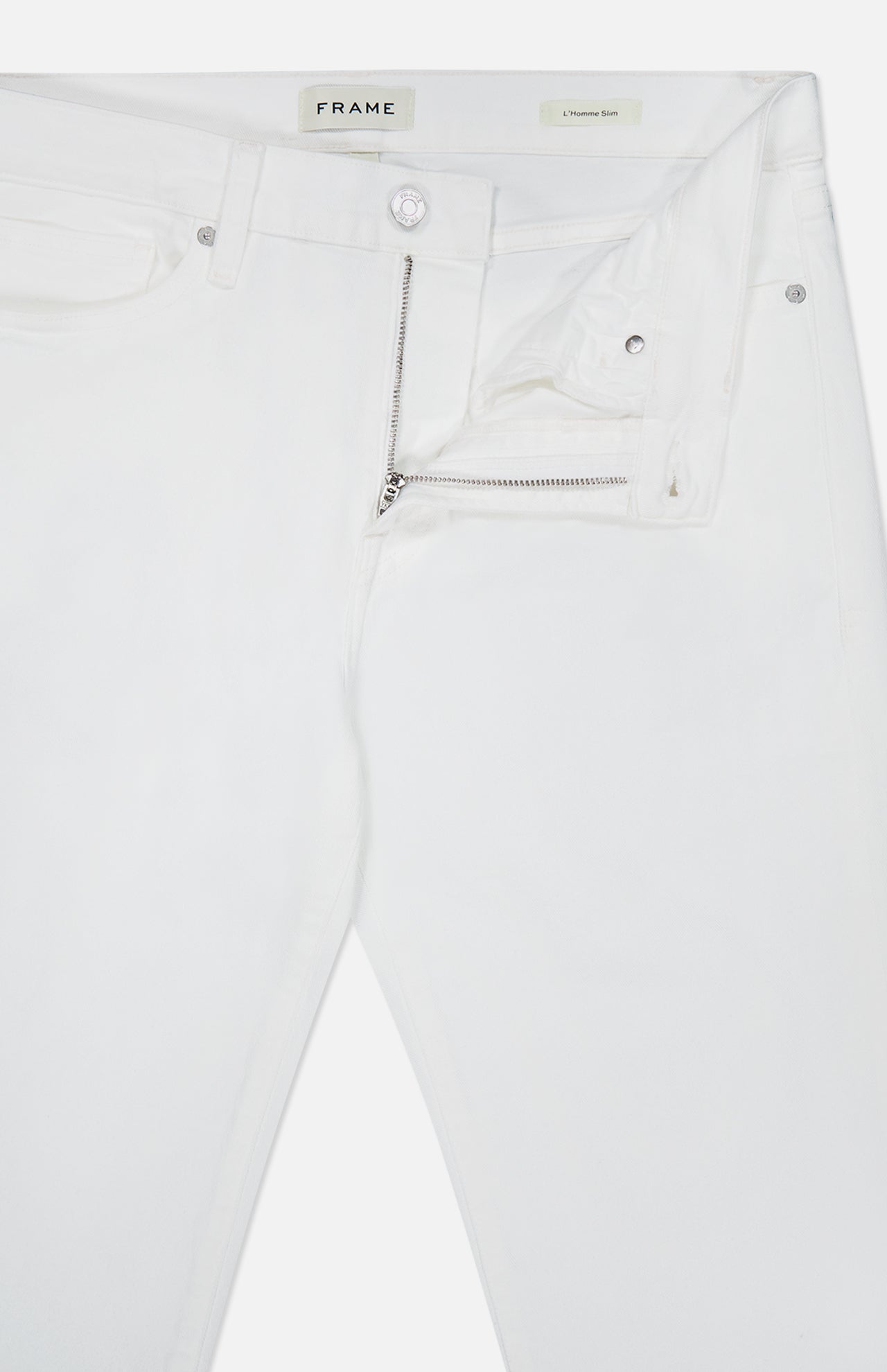 Introducing the L’Homme Slim Pant in Whisper White by Frame—crafted from premium stretch denim, these white jeans offer a slim fit silhouette with a partially unzipped fly and an open waistband that reveals the FRAME brand label inside.