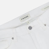 Close-up of the waistband and front pockets on the L’Homme Slim Pant in Whisper White by Frame, expertly crafted from premium stretch denim. Features include a metal button, an inner FRAME brand label, and a visible L’Homme Slim style tag.