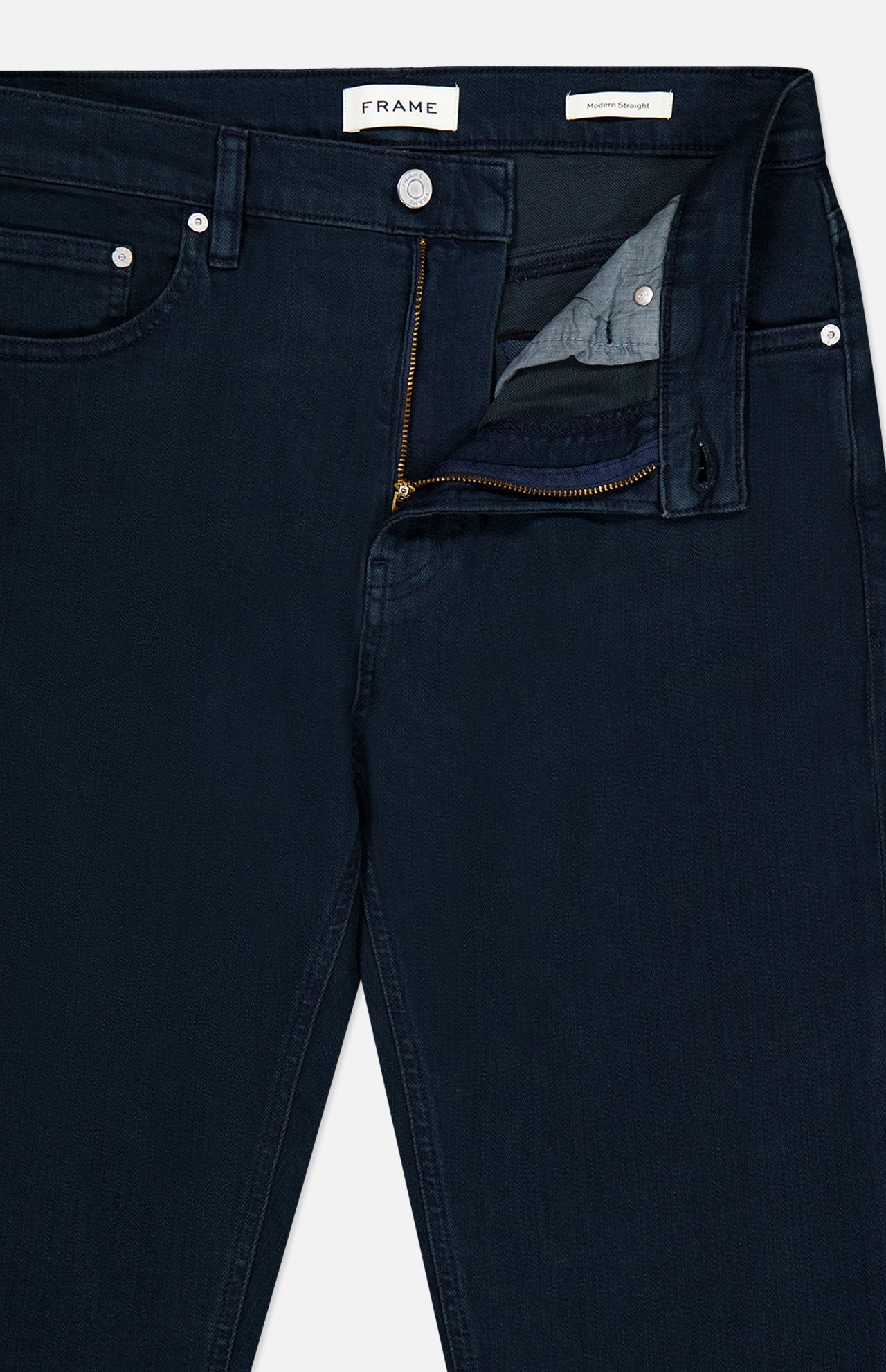 A close-up of the Frame Modern Straight Pant in Placid, featuring straight-leg comfort stretch denim in dark navy with a partially unzipped zipper and open waistband, highlighting the inside pocket and button details.