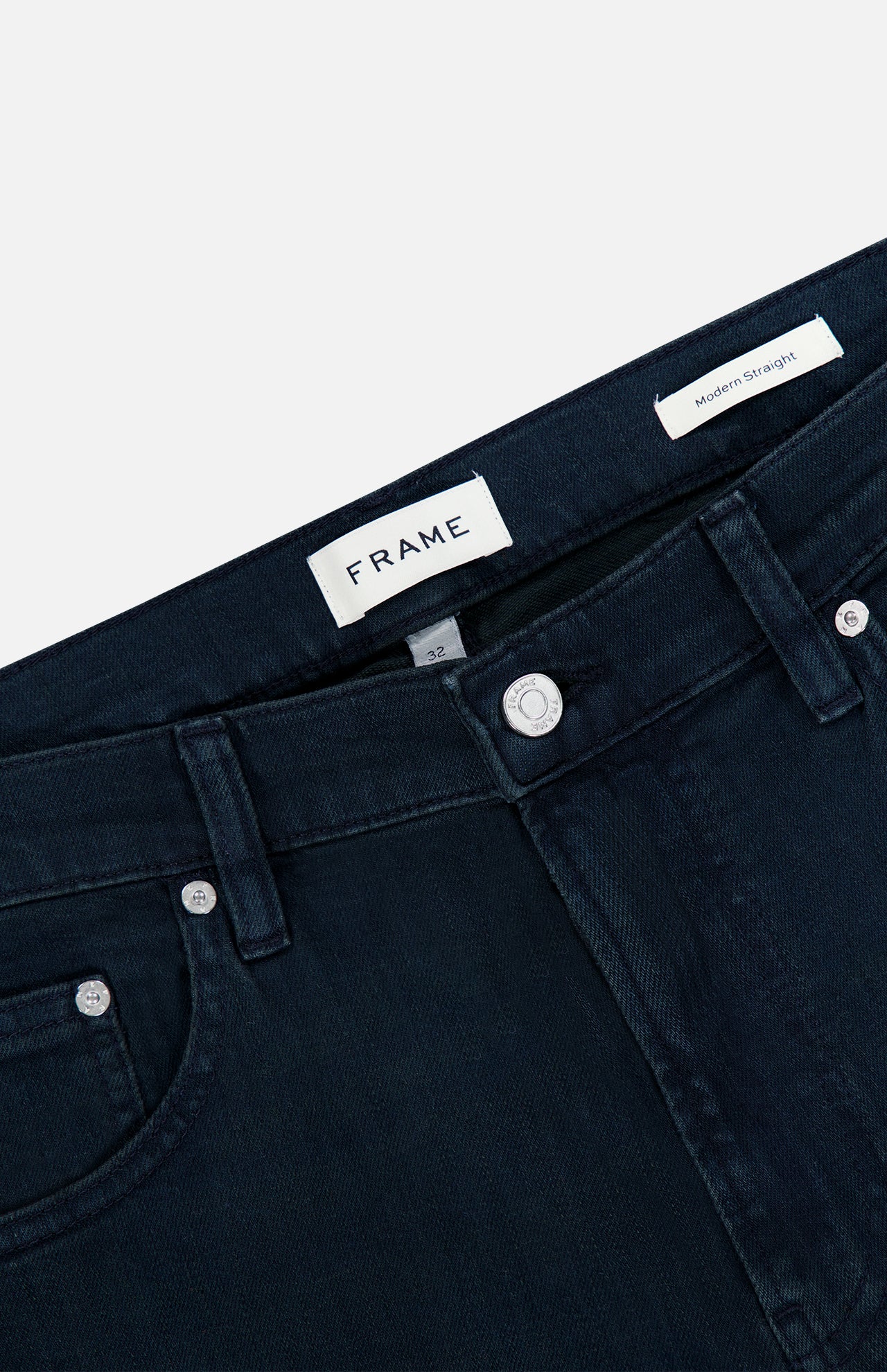 The Modern Straight Pant in Placid by Frame is crafted from comfort stretch denim in a dark blue wash, featuring silver buttons and rivets, belt loops, and visible FRAME and Modern Straight tags inside the waistband, shown on a plain white background.